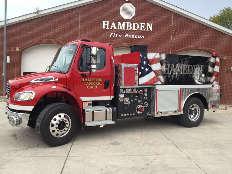 A red fire tanker truck labeled "Hambden Fire-Rescue" is parked in front of a brick building. The truck has the number 3638 and features an American flag design on its side.
