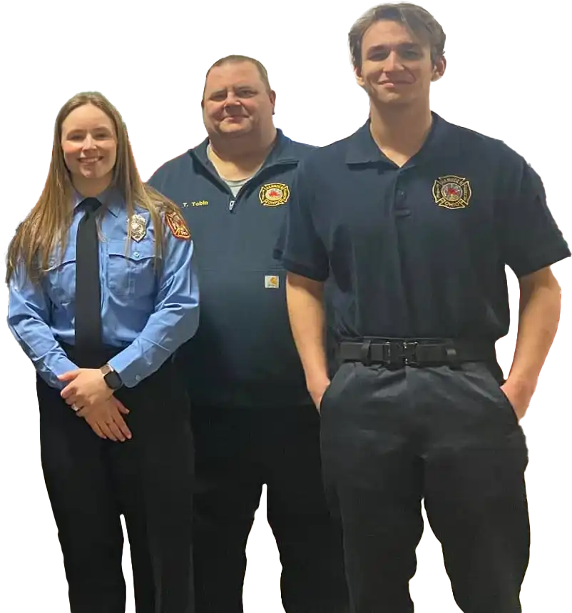Three people in firefighting uniforms stand smiling. One wears a blue shirt with a badge, the others wear black shirts with an emblem. They pose indoors against a gradient background.